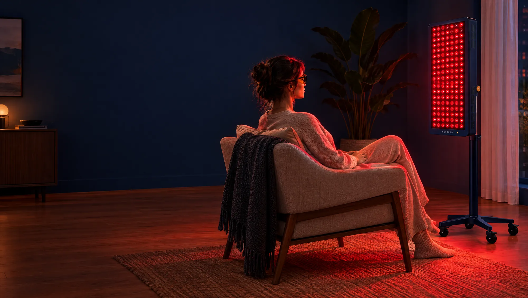 A person relaxing in a lounge chair in front of a Solbeam panel glowing warm red in a calm living room